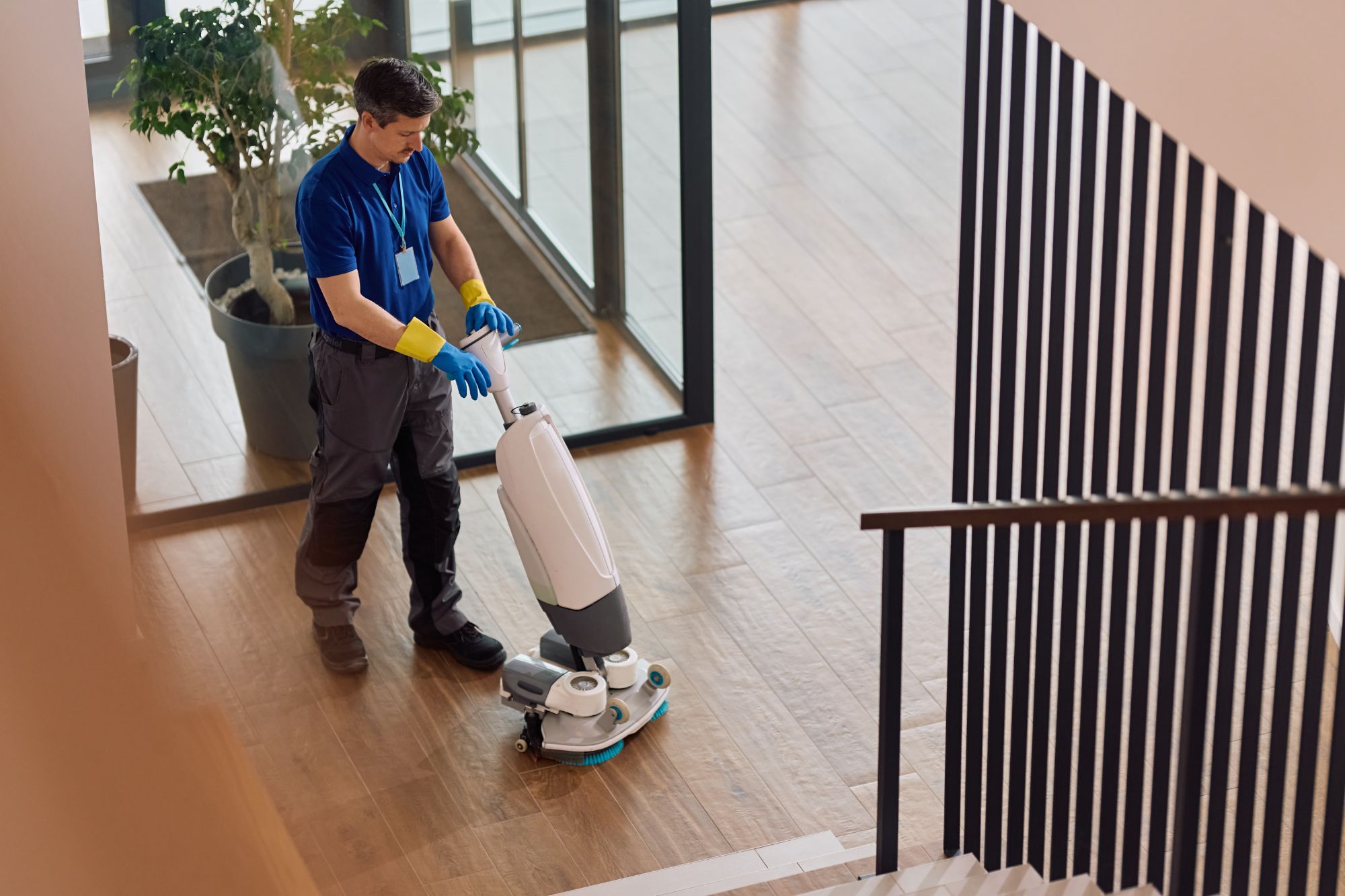 Professional cleaner using floor polisher in modern hallway with stairs